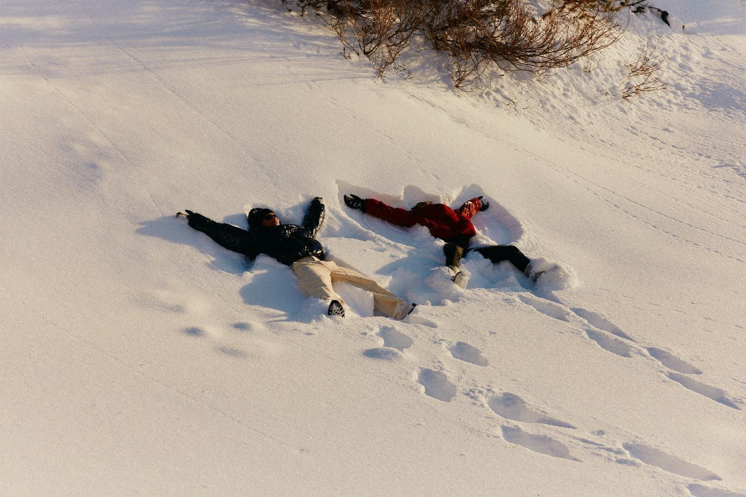 Two people lying in fresh snow in low winter sun.