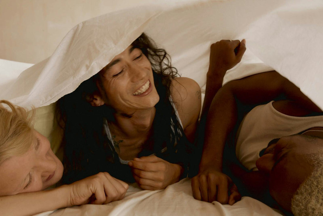 Three people laughing together under a linen duvet.