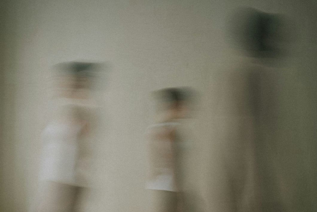 Figures moving through a pale room, caught in a long exposure.