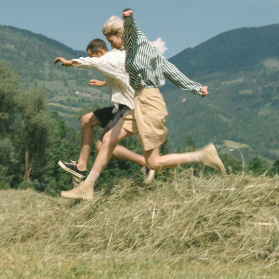 Two people jumping through a mown hayfield, mountains behind