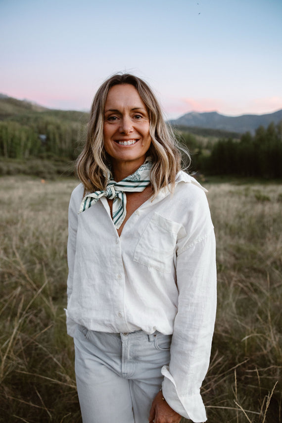 A woman in a white linen shirt standing in long grass at dusk