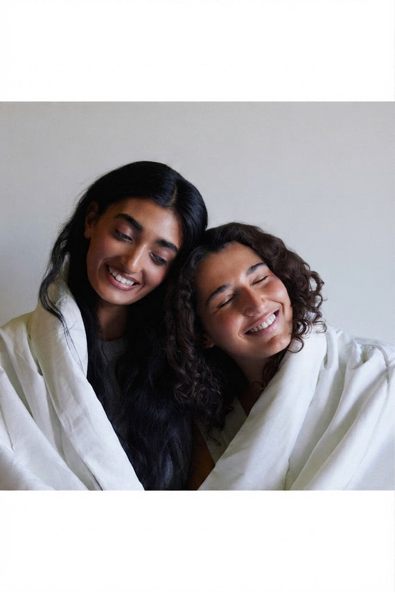Two women wrapped together in white linen, laughing