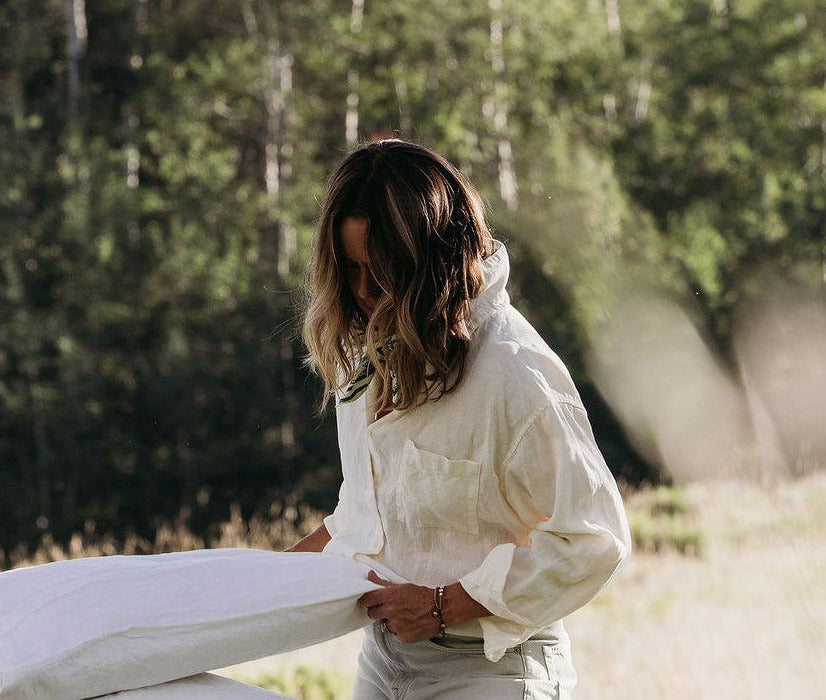 A woman carrying folded linen across a meadow, aspens behind her